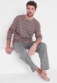 Camicia a maniche lunghe grigia a righe con scollo henley, abbinata a pantaloni grigi. Tessuto morbido, vestibilità rilassata, mostrata seduta su uno sfondo bianco.