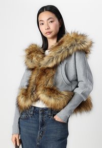 Γκρι κοντό sweatshirt με μεγάλο καφέ τεχνητό γιακά, με μακριά μανίκια και χαλαρή εφαρμογή. Φορεμένο πάνω από λευκό τοπ και μπλε τζιν φούστα.