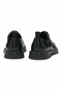 Black leather shoes with a smooth finish, rounded shape, and low-profile rubber soles. Features a small red accent on the heel tabs.