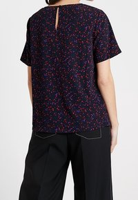 Navy blouse with a colorful abstract pattern, short sleeves, back keyhole detail, and a relaxed fit, paired with tailored black pants.