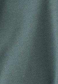 Tissu teal, doux, avec une texture lisse, présentant des variations subtiles de couleur et un motif légèrement chiné.