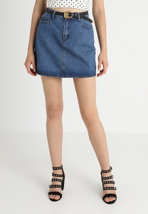 Denim-Minikleid in tiefblau, mit geradem Schnitt und fransigem Saum. Paar schwarze Sandalen mit Riemen, runden Nieten und offenem Zehenbereich.