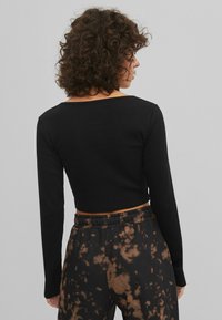 Svart ribbad långärmad croptopp med bred ringning, i kombination med svarta och bruna tie-dye-byxor. Mjuk textur och figurnära design.