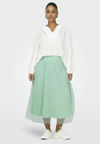 Biely dlhý rukáv blúzka s V- v�ýstrihom a horizontálnym prešívaním, kombinovaná s plisovanou mätovo zelenou sukňou a bielymi teniskami.