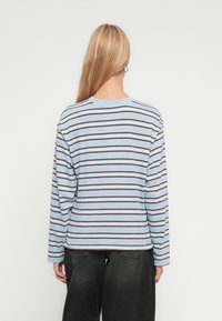 Μακρυμάνικη ριγέ μπλούζα σε ανοιχτό μπλε με καφέ οριζόντιες ρίγες, βαμβακερό ύφασμα, άνετη εφαρμογή, στρογγυλή λαιμόκοψη και ραφές ώμων που πέφτουν χαμηλά.