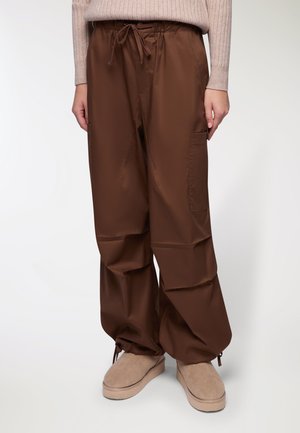 Pantaloni marroni, larghi e comodi, realizzati in un tessuto liscio, con una cintura elastica e un cordoncino, e con tasche laterali.