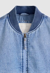 Šviesiai mėlynos spalvos džinsinė striukė su tamsiai mėlynu ribbiniu apykakliu ir priekinio užtrauktuko uždarymu, vidinėje apykaklės srityje matomas Levi Strauss & Co. ženklas.