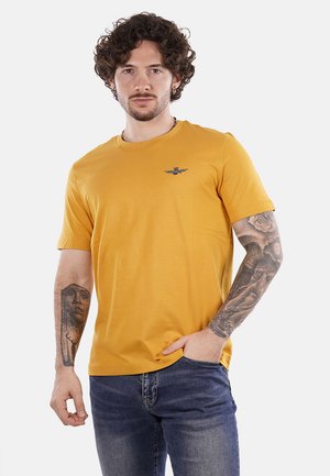 Geel T-shirt met korte mouwen en ronde halslijn, voorzien van een geborduurd logo op de linkerborst. Katoenen stof, soepele textuur, slim fit ontwerp.
