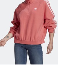 Pink fleece pullover with a half-zip, ribbed hem, and cuffs. Features white three-stripe accents on sleeves and an Adidas logo on the chest.