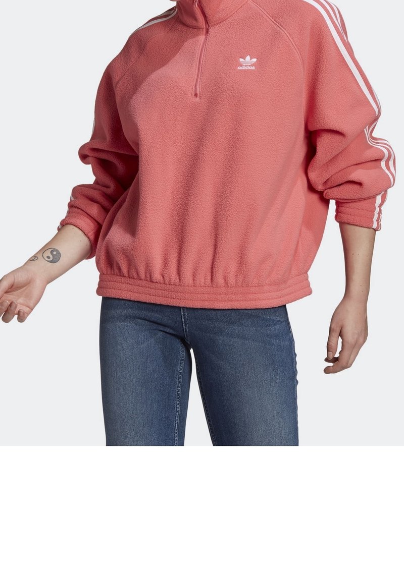 Pink fleece pullover with a half-zip, ribbed hem, and cuffs. Features white three-stripe accents on sleeves and an Adidas logo on the chest.