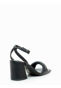 Sandalo nero con tacco alto a blocco largo, punta aperta e cinturino alla caviglia. Materiale in pelle liscia con design minimalista e hardware sobrio.