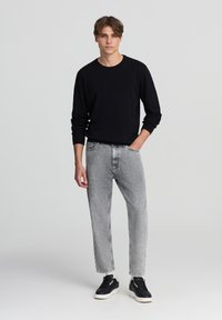 Maglietta nera a manica lunga, jeans grigi a gamba affusolata e sneaker nere. Design semplice, trama liscia, palette di colori neutra.