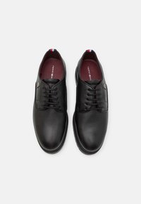 Chaussures habillées en cuir noir avec une finition texturée, design à lacets, bout arrondi, et un accent rouge, blanc et bleu au talon.