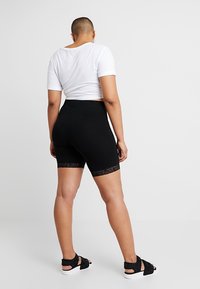 Mustat shortsit, joissa on pitsireunus helman ympärillä, suunniteltu tiukasti istuvaksi. Yhdistettynä valkoiseen lyhytlahkeiseen t-paitaan ja mustiin sandaaleihin.