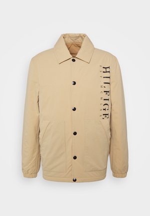 Beige button-up jacket with collar, elastic cuffs, two front pockets, and "HILFIGER EST. MCMLXX" printed vertically on the right chest.