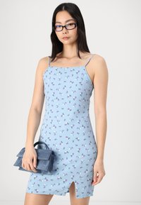 Μπλε φλοράλ φόρεμα με λεπτές τιράντες, που διαθέτει μια διακριτική μπροστινή σχισμή και υφασμάτινη υφή. Συνοδευόμενο από μια μικρή μπλε τσάντα.