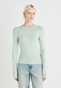 Mintgrønn langermet skjorte med rund hals og tettsittende design, laget av et glatt og mykt stoff. Kombinert med lyseblå jeans.