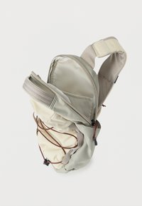 Συμπαγές μπεζ και ανοιχτό γκρι σακίδιο πλάτης με ανοιχτό φερμουάρ, ελαστικό καφέ κορδόνι στο μπροστινό μέρος και επενδυμένο ρυθμιζόμενο λουράκι με κλείσιμο Velcro.