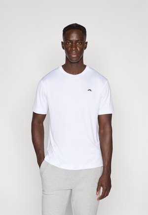 Wit T-shirt met korte mouwen en een ronde hals, met een klein zwart logo op de linkerborst. Gecombineerd met lichtgrijze joggingbroek.