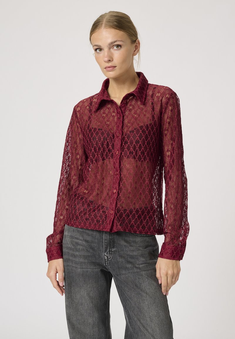 Burgundy lace button-up shirt with a diamond pattern, long sleeves, and a pointed collar, paired with dark gray jeans.