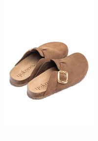 Sabots en suede marron avec une large sangle et une boucle carrée en or, dotés d'une semelle en liège texturée et d'un intérieur doux.