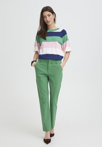 Haut en maille rayé aux tons bleu marine, vert, rose et blanc ; associé à un pantalon vert ajusté et des ballerines marron. Textures lisses, coupe décontractée.