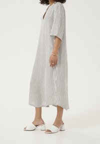 Robe en lin rayée avec un décolleté en V, des manches mi-longues, des fentes latérales, une coupe ample, portée avec des sandales blanches à talons blocs et bouts ouverts.