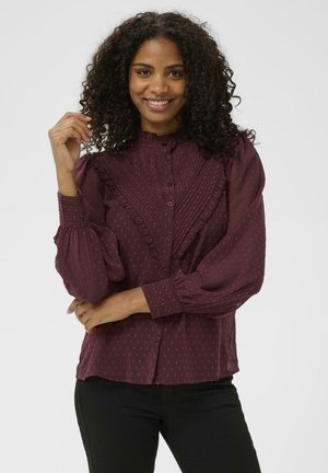 Burgunderfarbene Bluse mit gefälteltem Vorderteil, Rüschendetails und Punkten-Muster. Lange, gepuffte Ärmel mit Knopfmanschetten. Knopfverschluss.