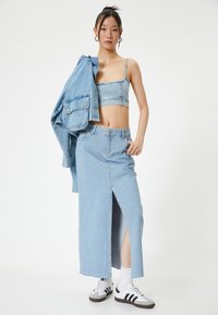 Vaaleansininen farkkuasu, joka sisältää crop topin ja pitkän hameen, jossa on edessä halkio. Asusteena on yhteensopiva takki ja urheilulliset tennarit.