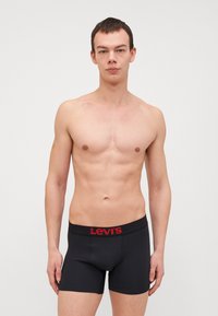 Svarta bomullskalsonger med en röd Levi's-logotyp på midjebandet, åtsittande design, slät textur och längd till mitten av låret.