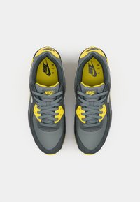 Gray and yellow Nike Air sneakers, viewed from above, featuring a textured surface, laces, and branding on the tongue and insole.