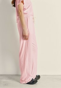 Ensemble de détente en coton rose comprenant un t-shirt ample et un pantalon large avec une taille élastique et un cordon de serrage, associé à des baskets noires.