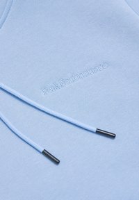 Lys blå hoodie med en blød tekstur. Har "PeakPerformance" broderi og matchende snor med sorte metalspidser.
