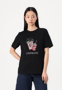 Zwarte katoenen t-shirt met korte mouwen, voorzien van een grafische afbeelding van rode en witte popcornemmers en een gestreepte drank, met de tekst "CINEMATIC" eronder.