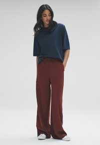 Námornícky modré tričko s krátkymi rukávmi v kombinácii s voľnými burgundskými nohavicami so bočnými pruhmi a bielymi teniskami. Hladká textúra látky.