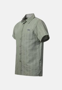 Chemise vert clair à manches courtes avec des rayures verticales texturées et une poche poitrine étiquetée "Seaside" sur fond blanc.