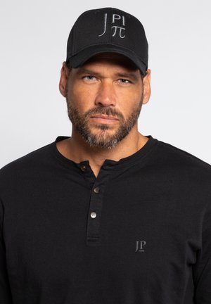 Schwarzes langärmliges Shirt mit Knopfleiste und kleinem Logo auf der Brust. Schwarze Kappe mit weißen gestickten Initialen und Symbolen.