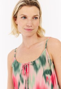 Top na cienkich ramiączkach w różowym, zielonym i białym wzorze tie-dye. Posiada zaokrąglony dekolt oraz sznurek w centrum z przodu.