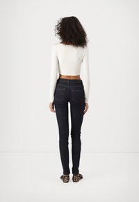 Σκούρο μπλε τζιν με στενή εφαρμογή και πίσω τσέπες, συνδυασμένο με ένα λευκό κοντομάνικο τοπάκι με μακριά μανίκια. Λεπτομέρειες περιλαμβάνουν ραφές και υφή υλικού.