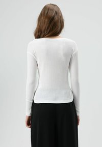 Wit geribbeld langärmelig topje met een rond halslijn, voorzien van een aansluitend silhouet en textuurstof, gecombineerd met zwarte broek met wijde pijpen.