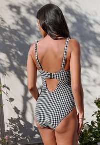 Schwarz-weiß kariertes Badeanzug-Einteiler mit verstellbaren Trägern, offenem Rückendetail und hoch geschnittenen Beinen, aus strukturiertem Stoff gefertigt.