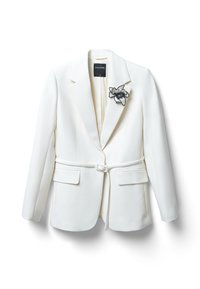 Weißer maßgeschneiderter Blazer mit Reverskragen, taillierter Taille und Fronttaschen. Mit einer schwarzen Blumenbrosche auf der linken Seite.