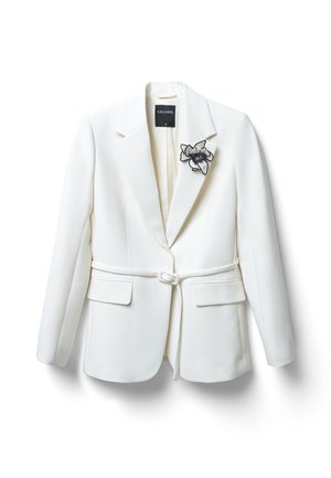 Blazer bianco su misura con colletto a punta, vita cintata e tasche frontali. Presenta una spilla floreale nera sul lato sinistro.