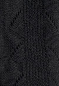 Svart stickad tyg med ett texturerat zickzackmönster, med en medelhårdhet och en mjuk, fluffig yta genom hela.