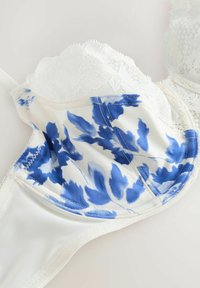 En spetstrimlad vit bh med ett blått blommönster på en krämfärgad botten, med en slät tygkvalitet och detaljerad sömnad runt kuporna och kanterna.