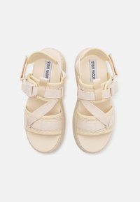 Beige sandals with thick cross-straps, a textured woven design, and adjustable buckle detail. Soft, lightweight material and rubber soles.