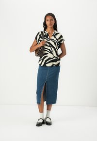 Haut à manches courtes en V couleur crème avec des rayures zèbre noires, associé à une jupe en denim longueur genou avec une fente à l'avant. Sac à main marron inclus.