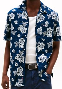 Short-sleeve button-up shirt in dark blue with white floral pattern. Features a chest pocket and a small logo tag. Made of lightweight fabric.