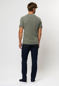 Tricou gri cu mânecă scurtă, cu textură canelată, asortat cu blugi de un albastru închis. Are guler rotund și o siluetă ajustată.