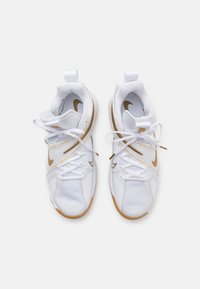 Baskets blanches avec une tige en maille texturée, un swoosh Nike doré et une semelle en caoutchouc brun clair. Comprend des lacets ajustables et des languettes de traction.